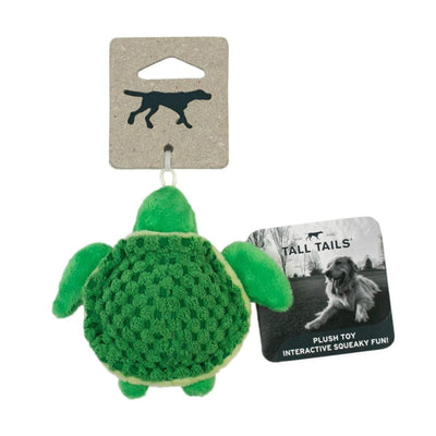 Green plush turtle dog toy with textured shell, hanging from a cardboard tag featuring a dog silhouette and brand name.