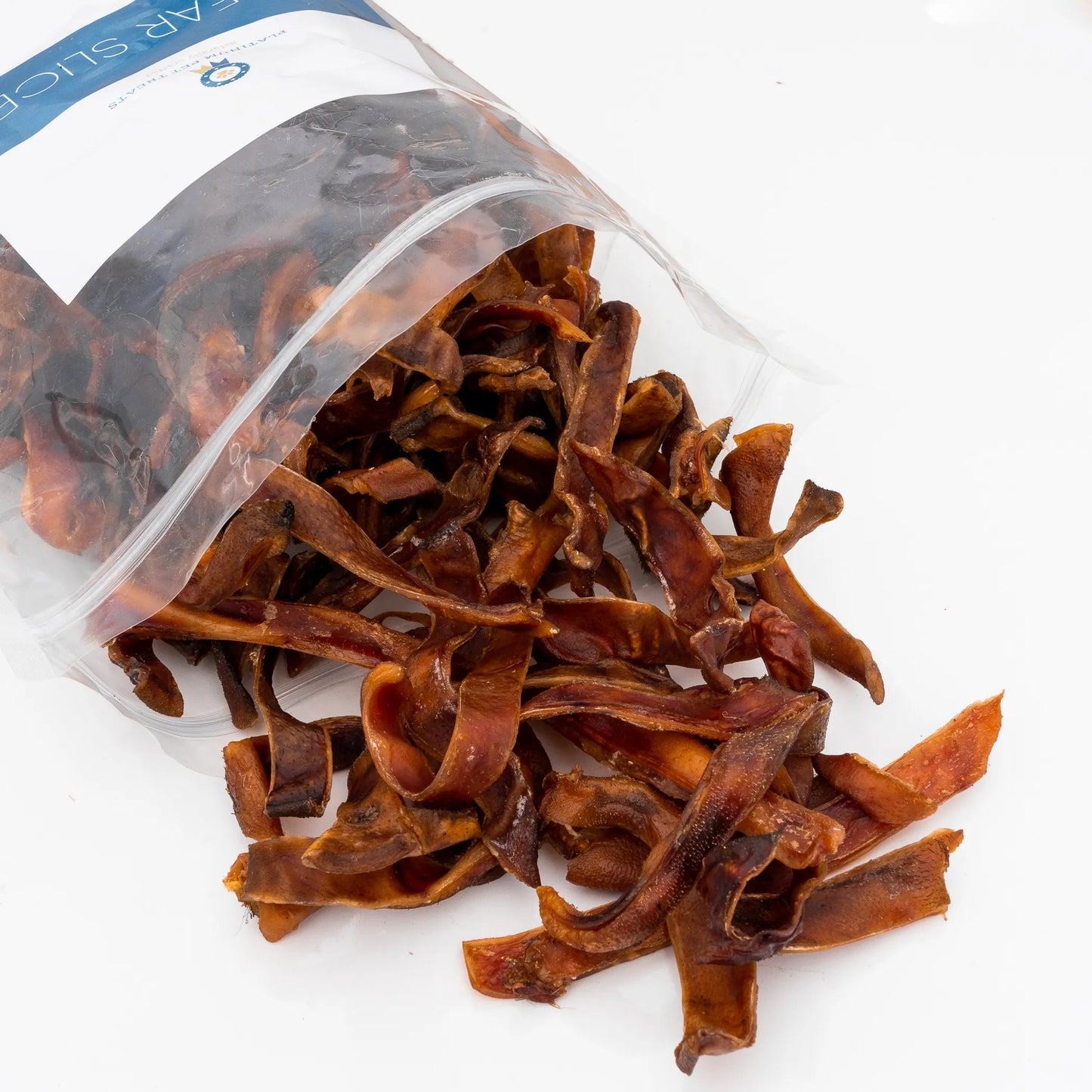 Platinum Pet Treats - Sliced Pig Ear spilling from opened clear resealable pouch on white background