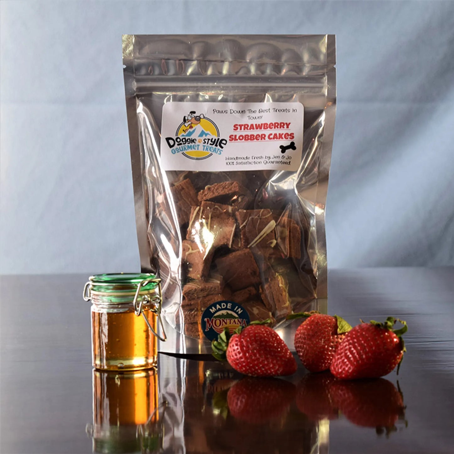 Strawberry Slobber Cakes dog treats package with fresh strawberries and a small jar of honey on table surface