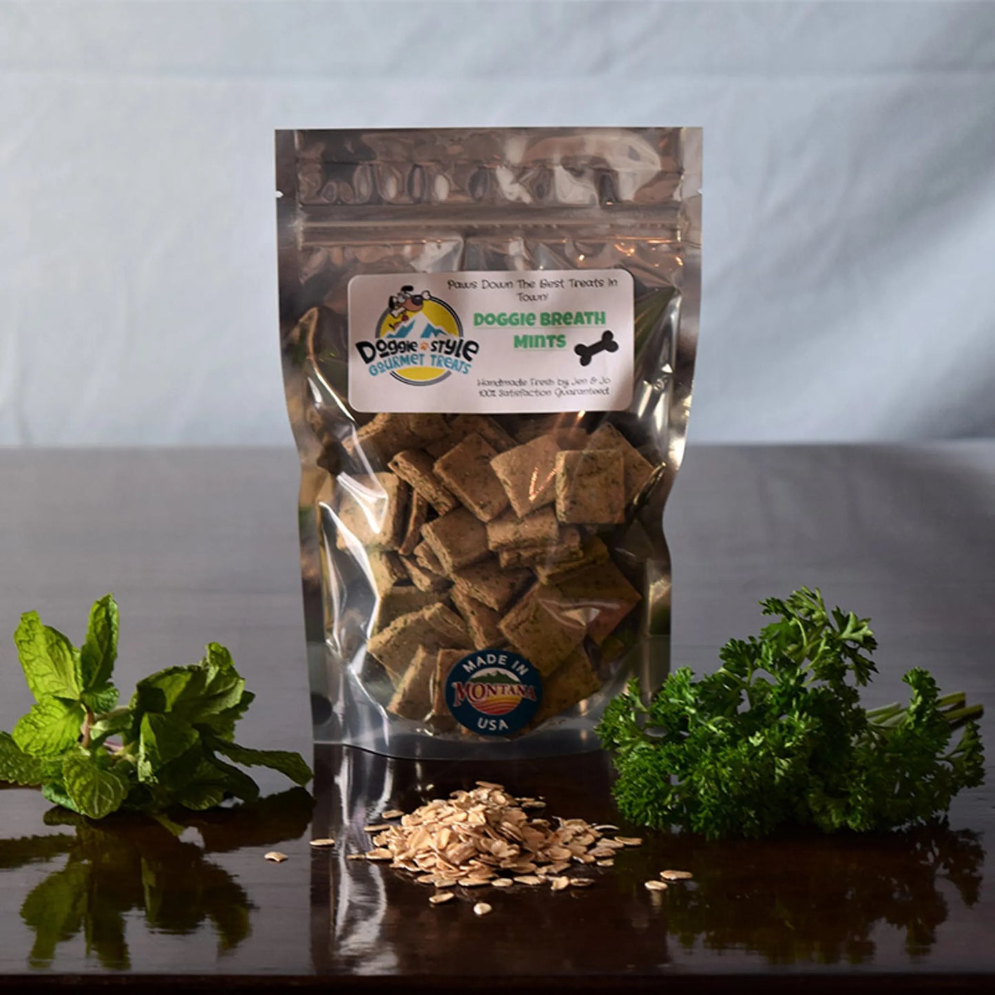 Doggie Breath Mints pet treats in clear resealable bag with oats, fresh mint, and parsley on wooden surface