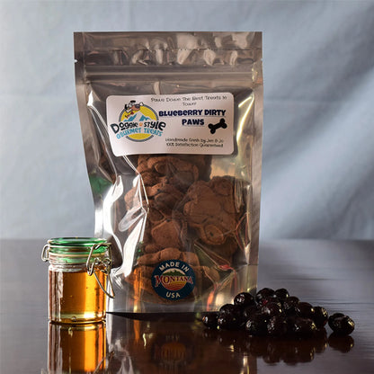 Blueberry Dirty Paws dog treats in clear resealable bag with honey jar and fresh blueberries on table