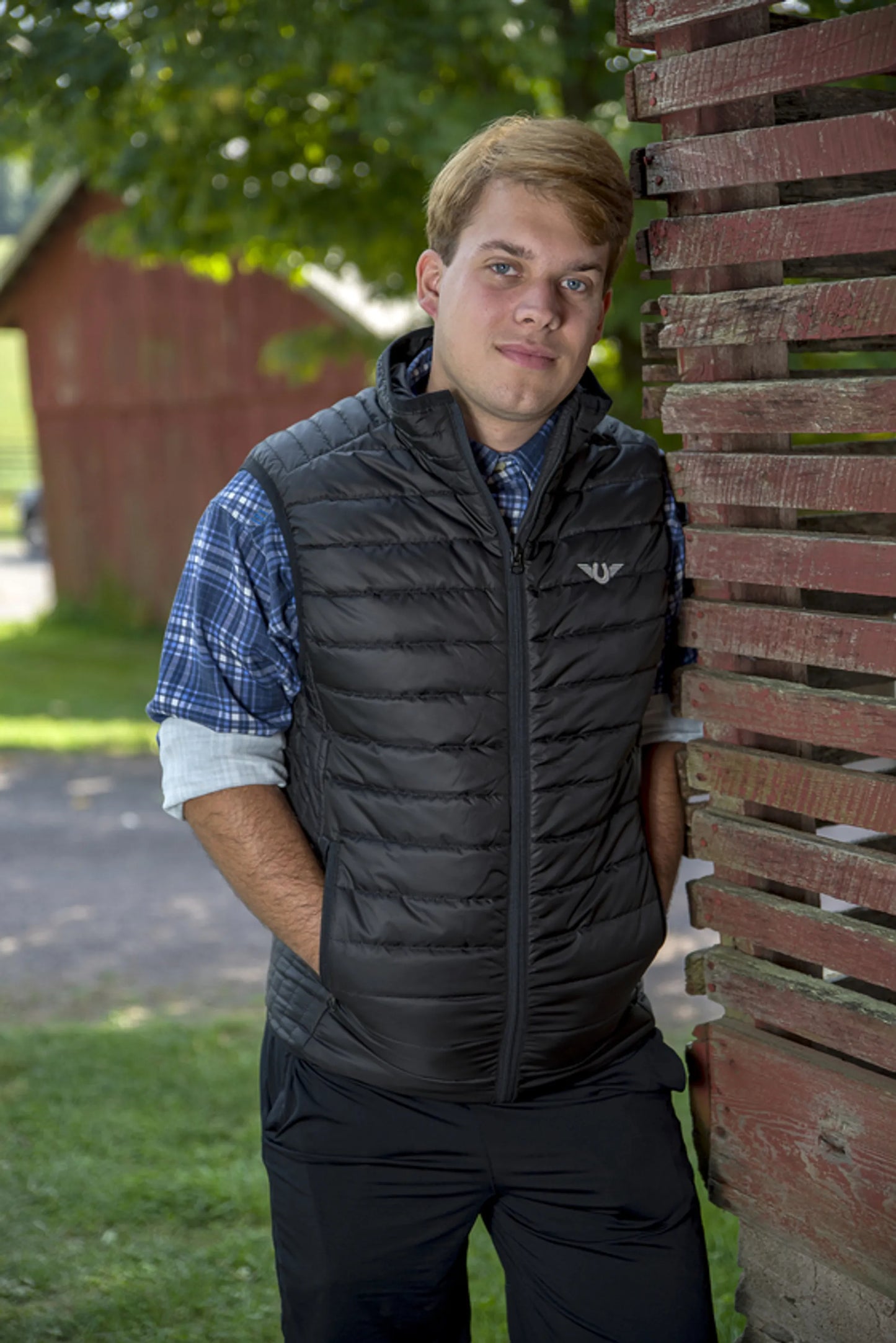 Man wearing black TuffRider Men's Zima Vest outdoors leaning against a weathered wooden fence in rural setting