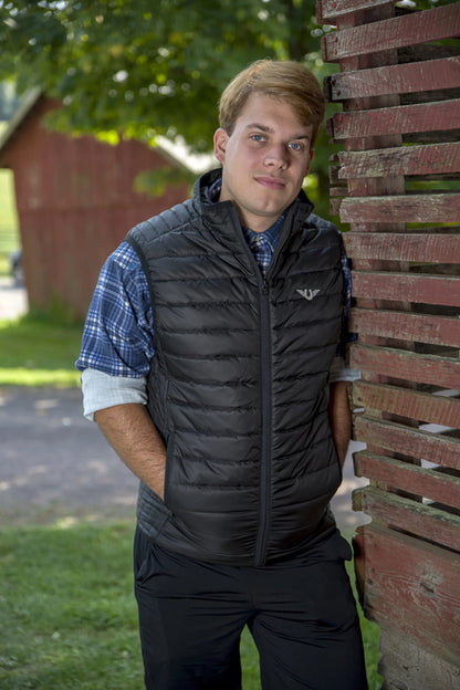 Man wearing a black TuffRider Men's Zima Vest outdoors leaning against a rustic red wooden fence