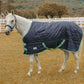 White horse wearing a navy blue TuffRider Kozy Komfort Stable Blanket standing in a fenced pasture.