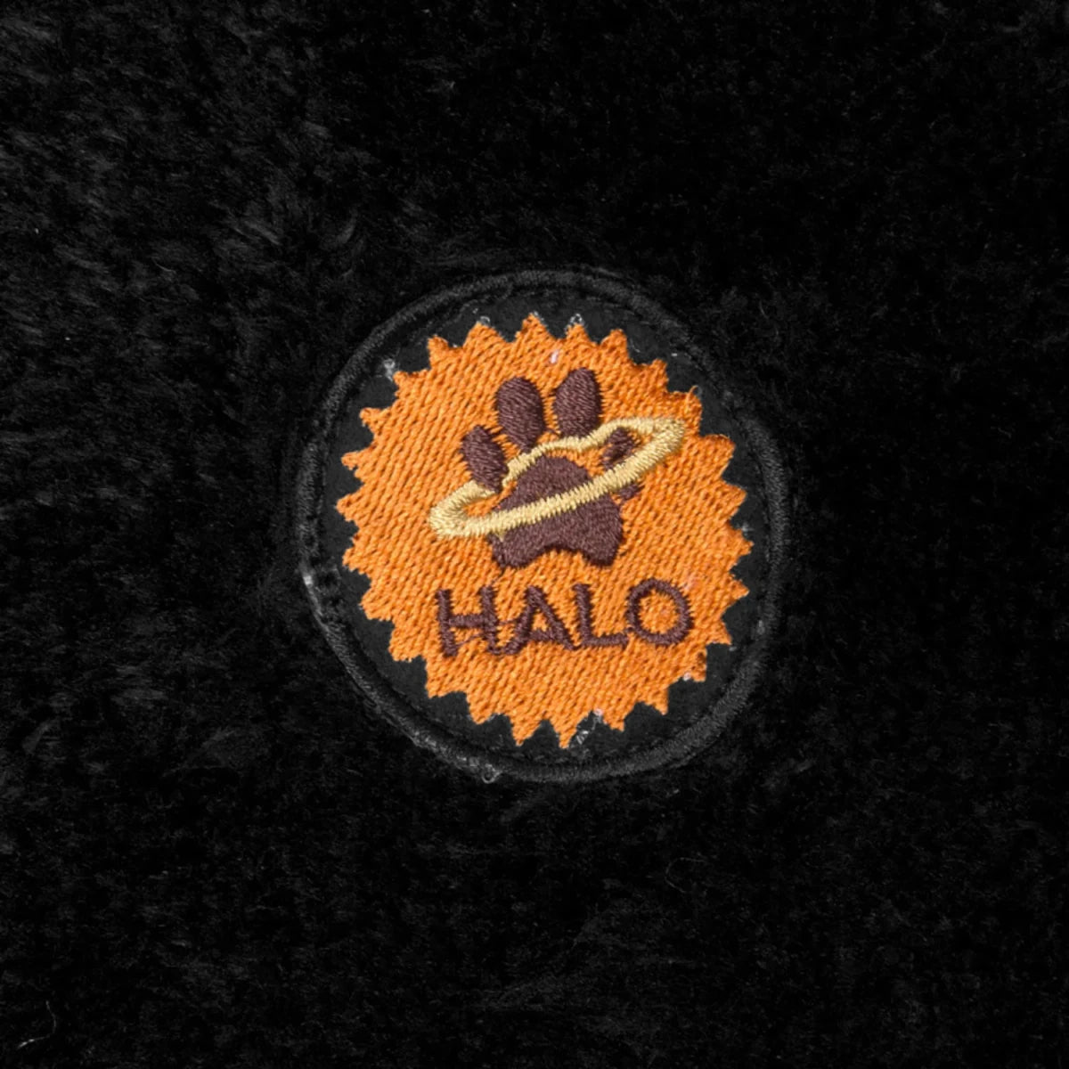 Close-up of embroidered halo paw logo on black fabric of Round Dog Bed - Quilted Plush Bed with Removable Washable Cover.