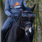 Horse wearing eQuick eVysor transparent protective eyewear ridden by rider in outdoor wooded setting