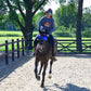 Rider wearing eQuick eVysor transparent reflective gear on horse in outdoor fenced arena on sunny day