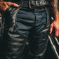 Close-up of black leather chaps worn over blue jeans, featuring belt and spandex detailing, 6130.00 - Unisex Ultra 4-Pocket Chaps with Spandex