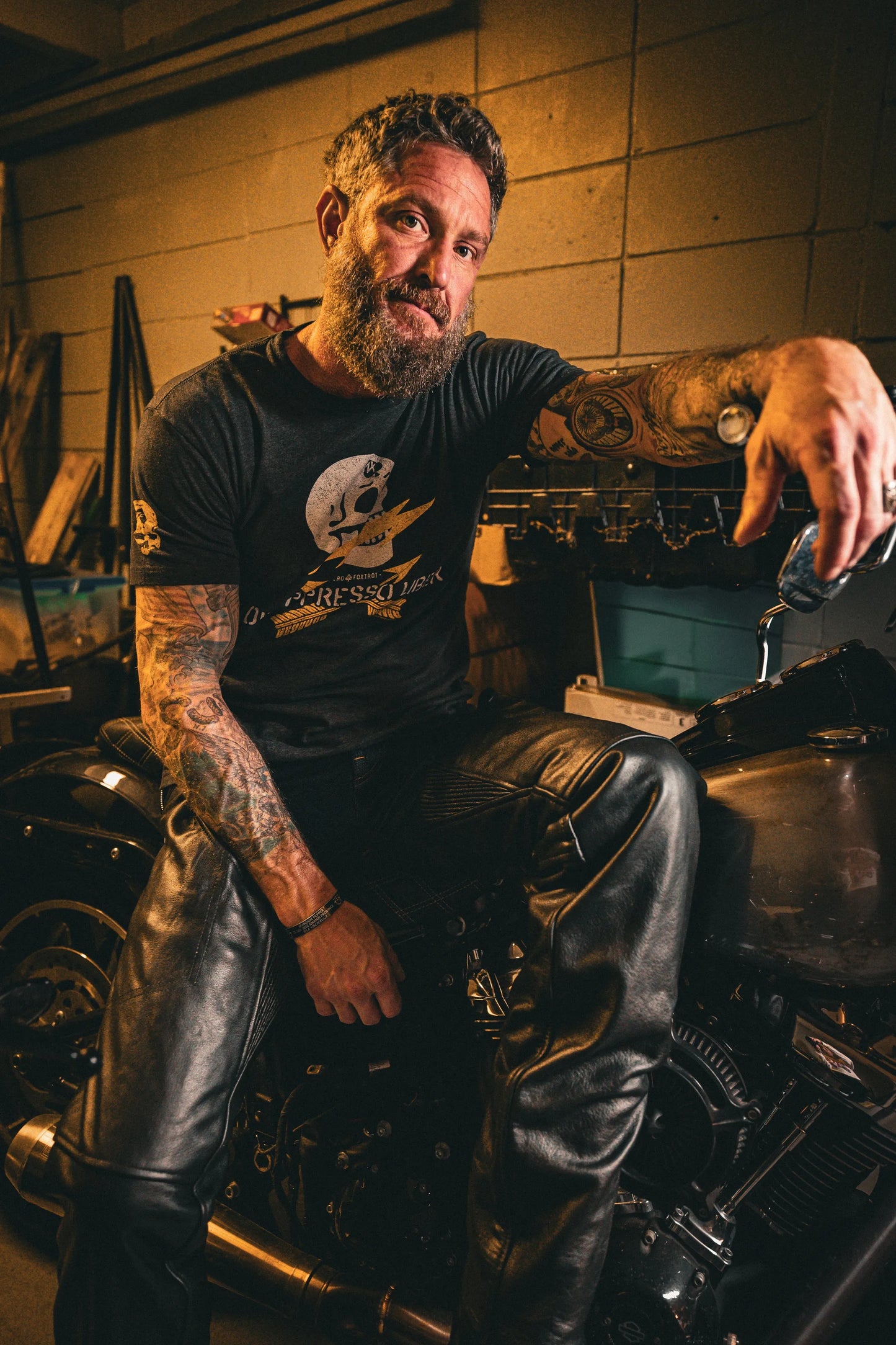 Man sitting on motorcycle wearing 7145.K - Unisex Premium Leather 4-Pocket Chaps with Spandex in dimly lit garage