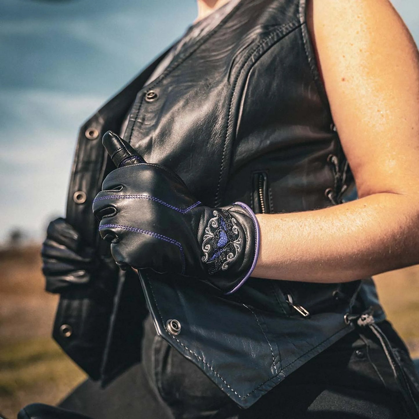 8144.17 - Ladies Full Finger Gloves in black leather with decorative stitching worn with a black leather vest outdoors