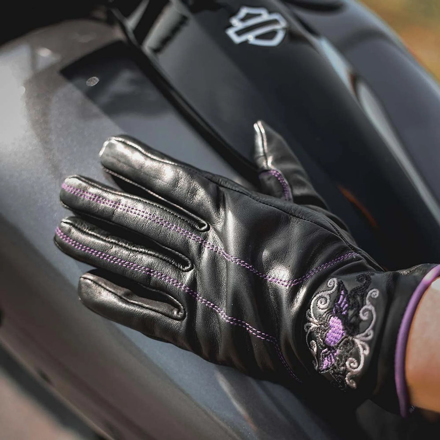 8144.17 - Ladies Full Finger Gloves in black leather with purple stitching and embroidered cuff detail on motorcycle tank