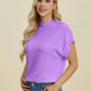 Woman wearing a lilac Double Take Full Size Mock Neck Short Sleeve Sweater with ribbed neckline and cuffs standing against a beige background