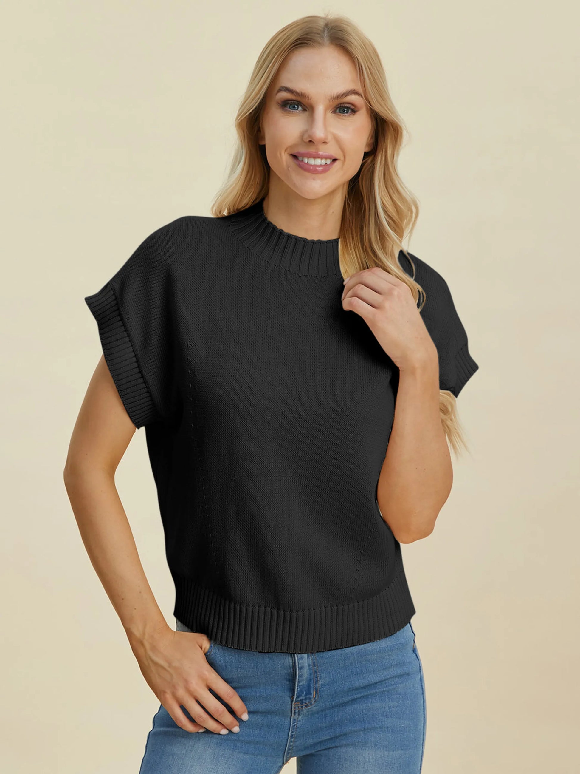 Woman wearing black Double Take Full Size Mock Neck Short Sleeve Sweater with ribbed details and blue jeans on beige background