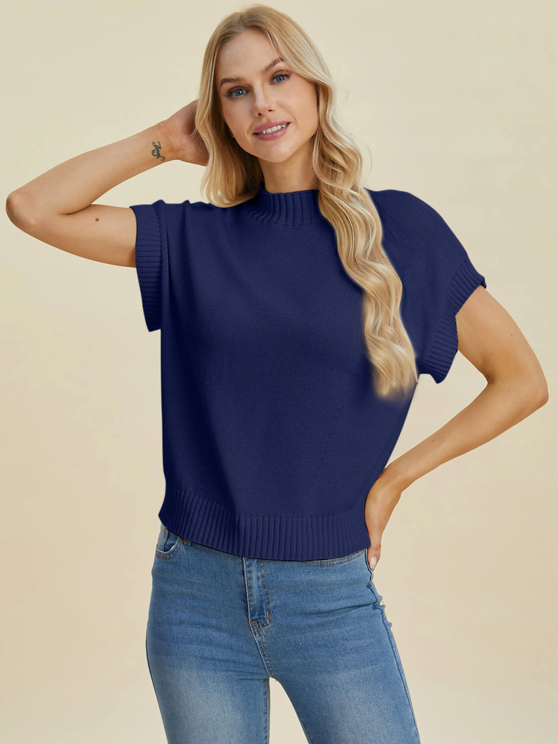 Woman wearing navy Double Take Full Size Mock Neck Short Sleeve Sweater paired with blue jeans against beige background