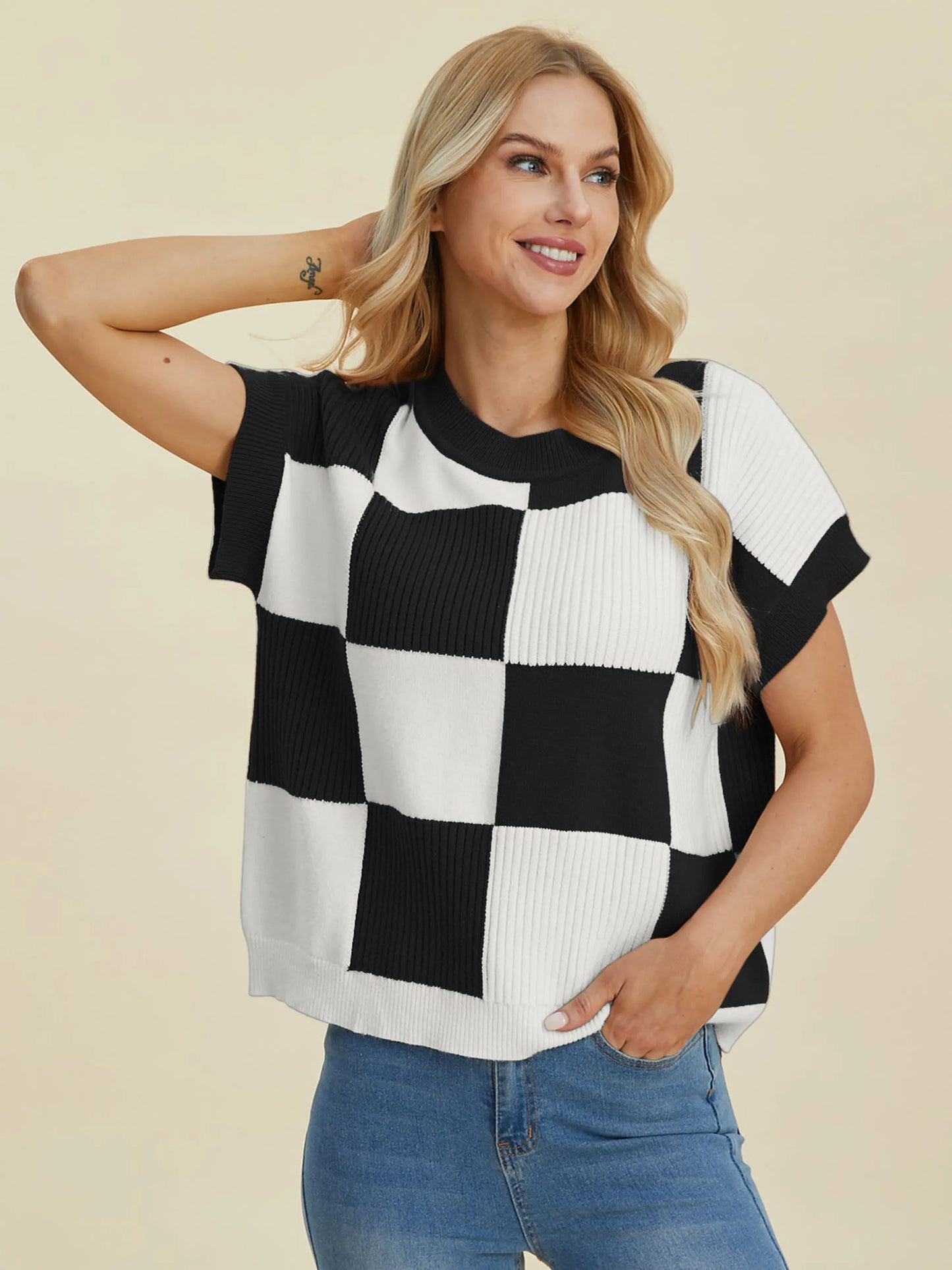 Woman wearing a black and white checkered knit top smiling, styled as Double Take Full Size Checkered Round Neck Short Sleeve Sweater