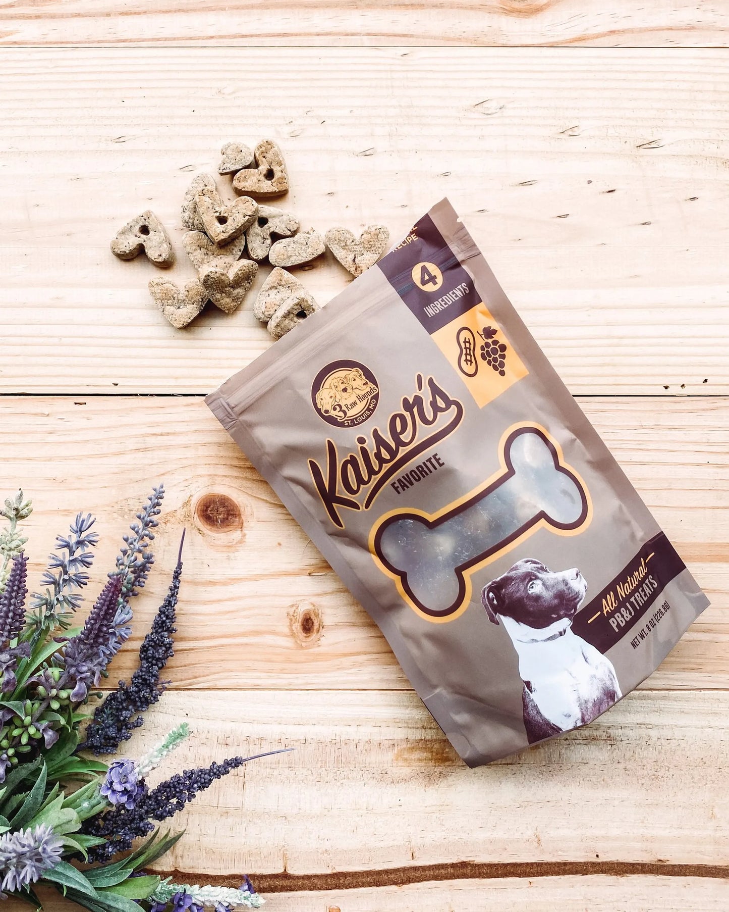 Kaiser's Favorites Dog Treats bag with heart-shaped treats on wood surface near purple flowers in pet supplies setting