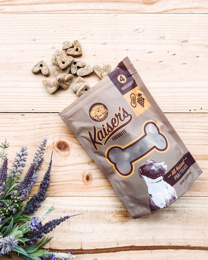 Kaiser's Favorites Dog Treats bag with heart-shaped treats on wood surface near purple flowers in pet supplies setting