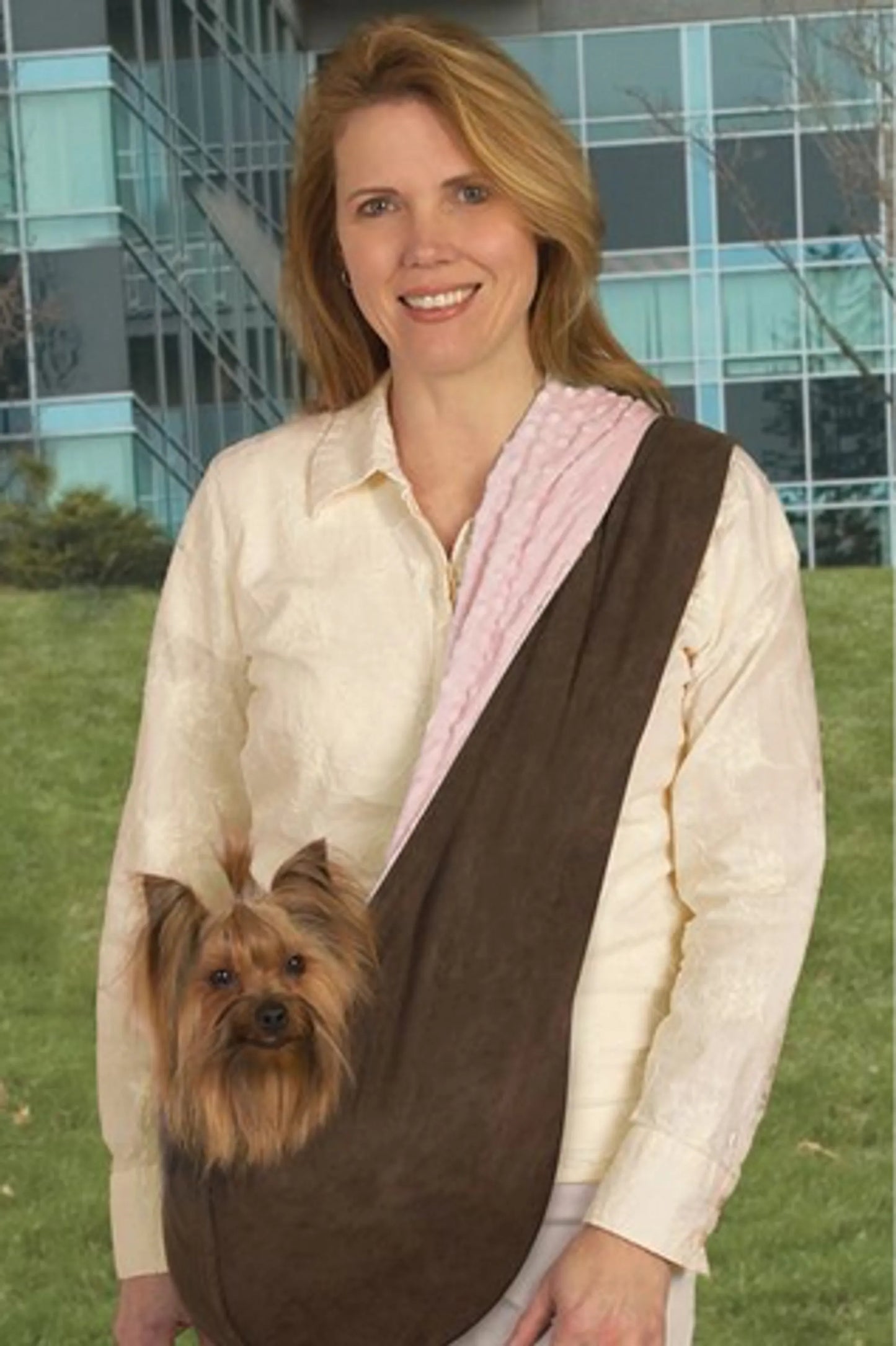 Woman wearing ESC Reversible Sling Pet Carrier holding small brown dog outdoors near modern building.